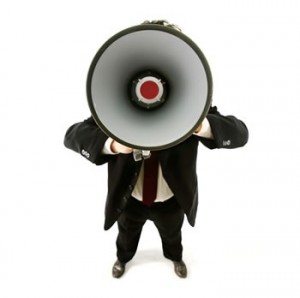 A man in a suit shouting into an oversized megaphone